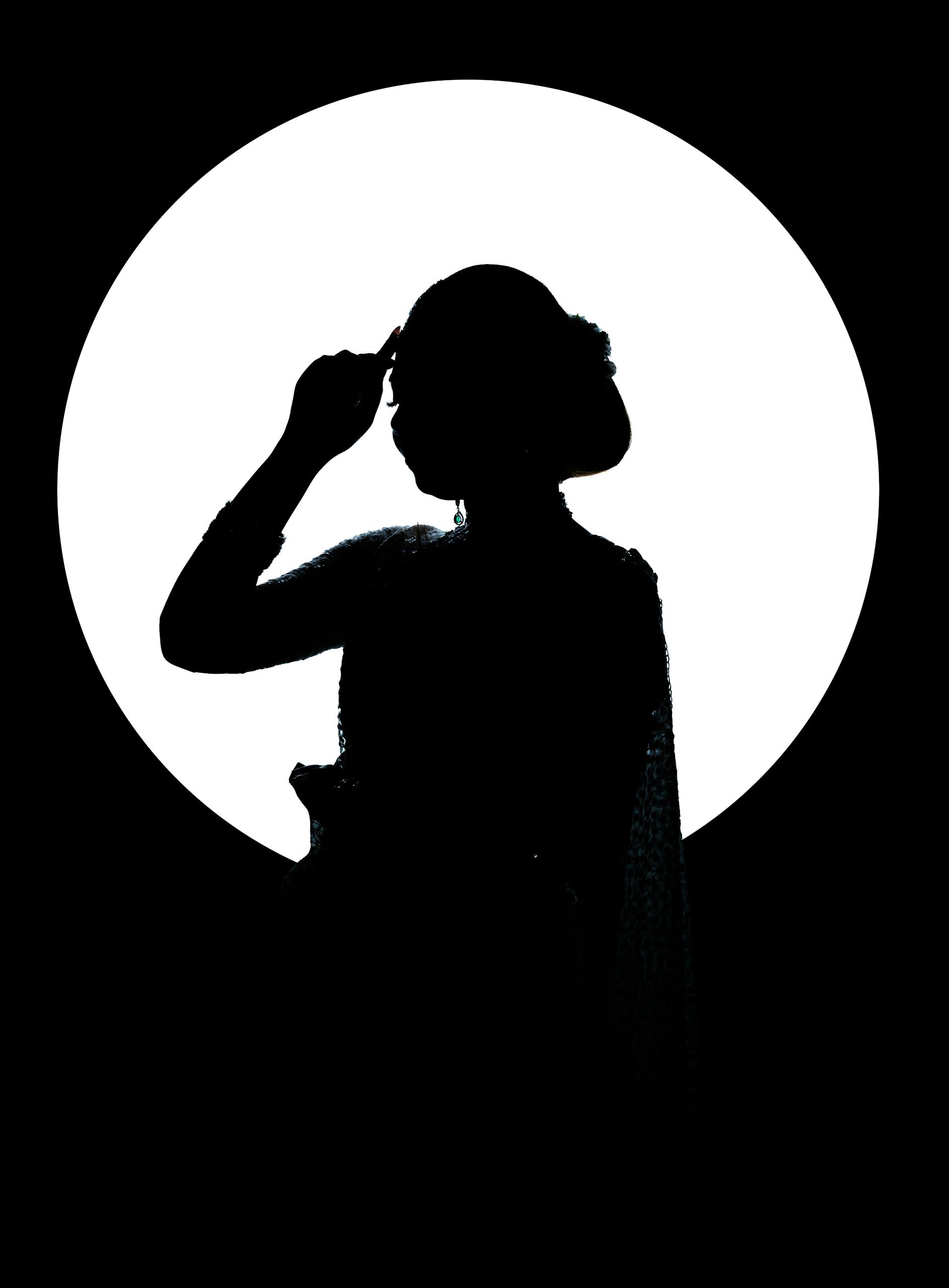 Silhouetted figure in artistic pose against a bright moon-like backdrop.